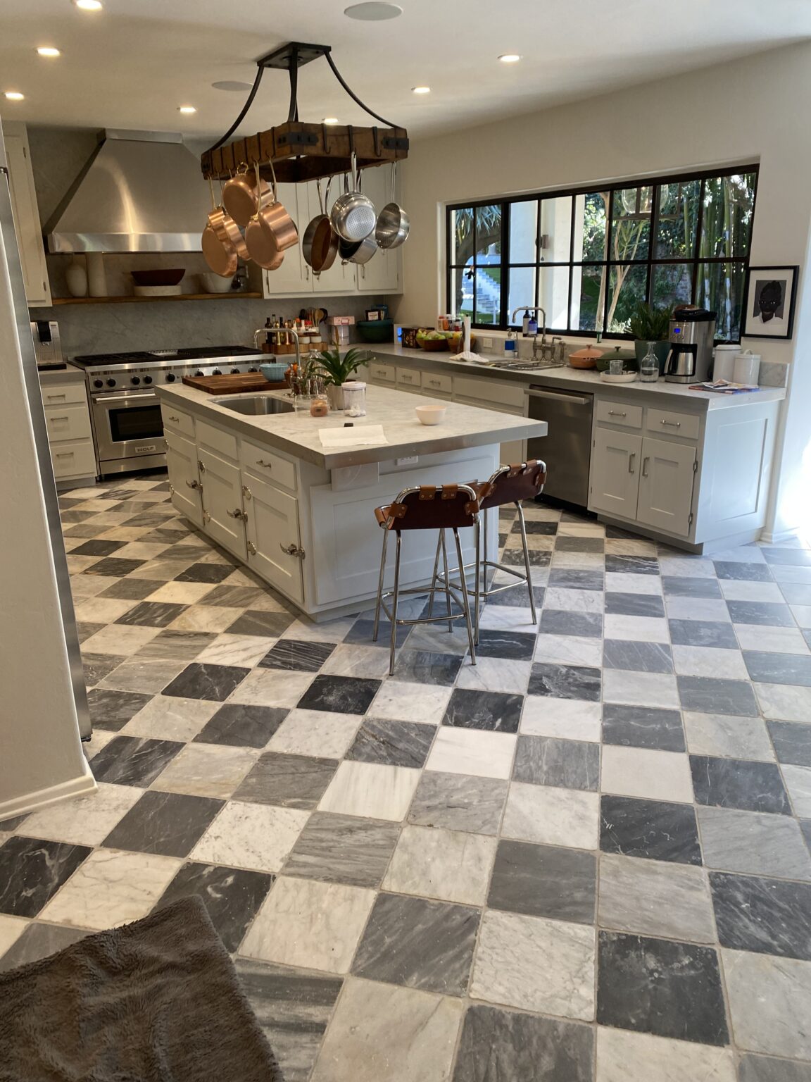 Kitchen with white shaker cabinets, a marble island, a copper pot rack and a checkerboard marble floor