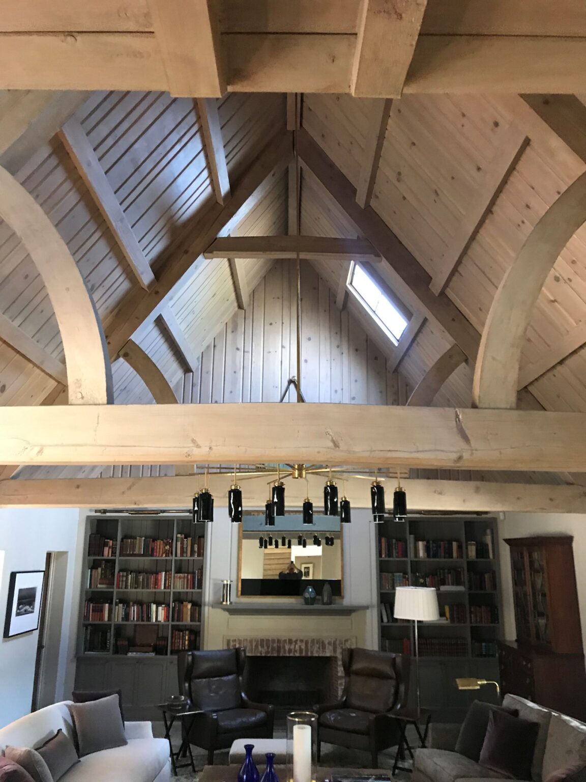 Great room with a vaulted timber-frame ceiling, built-in bookshelves, a brick fireplace and leather wingback chairs