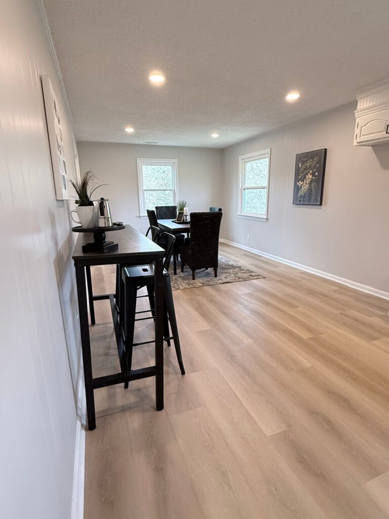 Outdated kitchen before renovation showing checkerboard flooring, mismatched dining room floor, old cabinets, dated appliances, and single light fixture