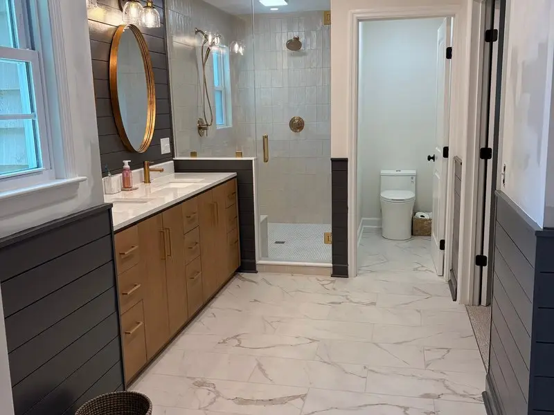 Primary bathroom with double wood vanity, gold hardware and glass shower