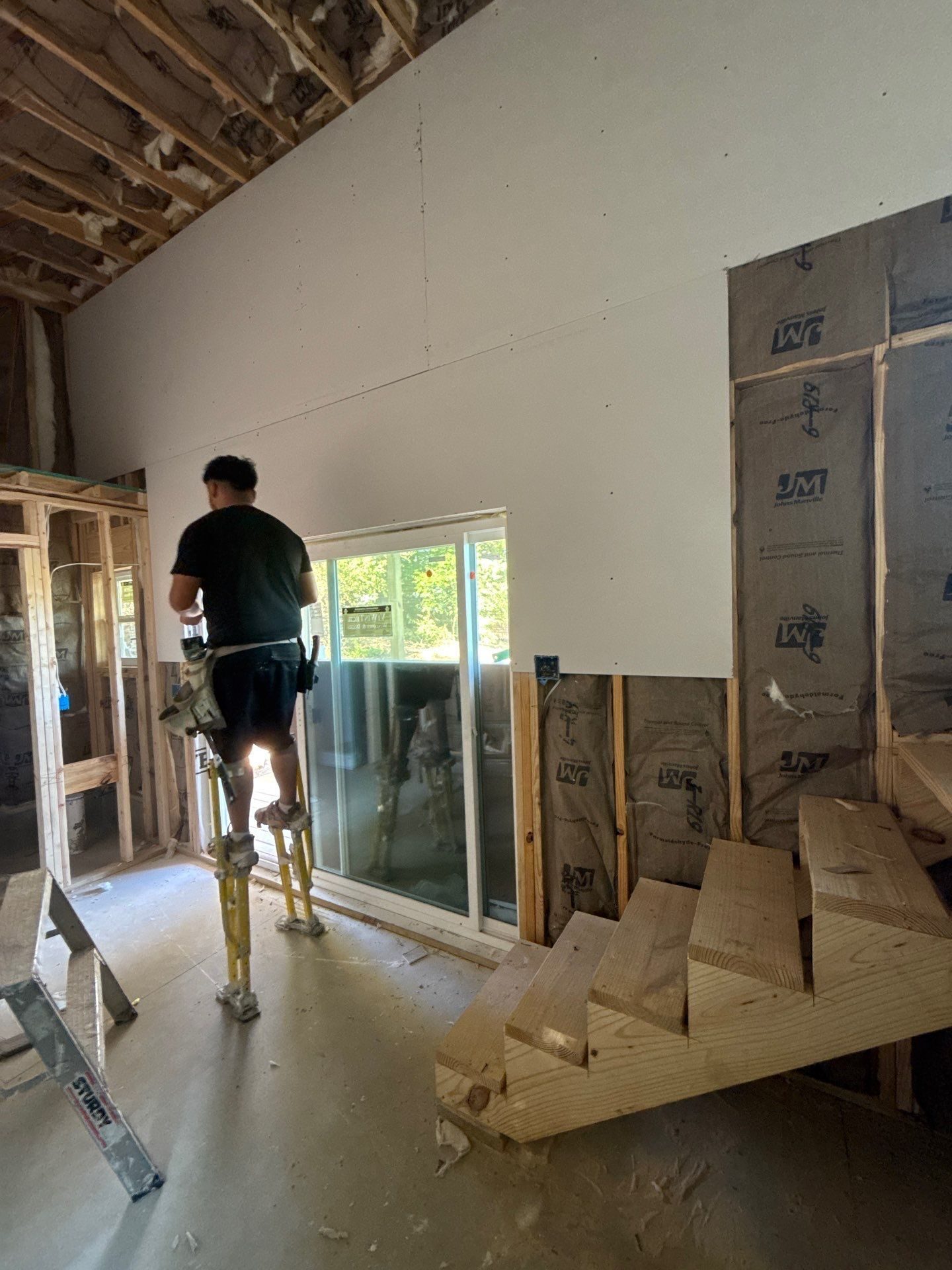 Crew member on stilts installing drywall in an ADU under construction
