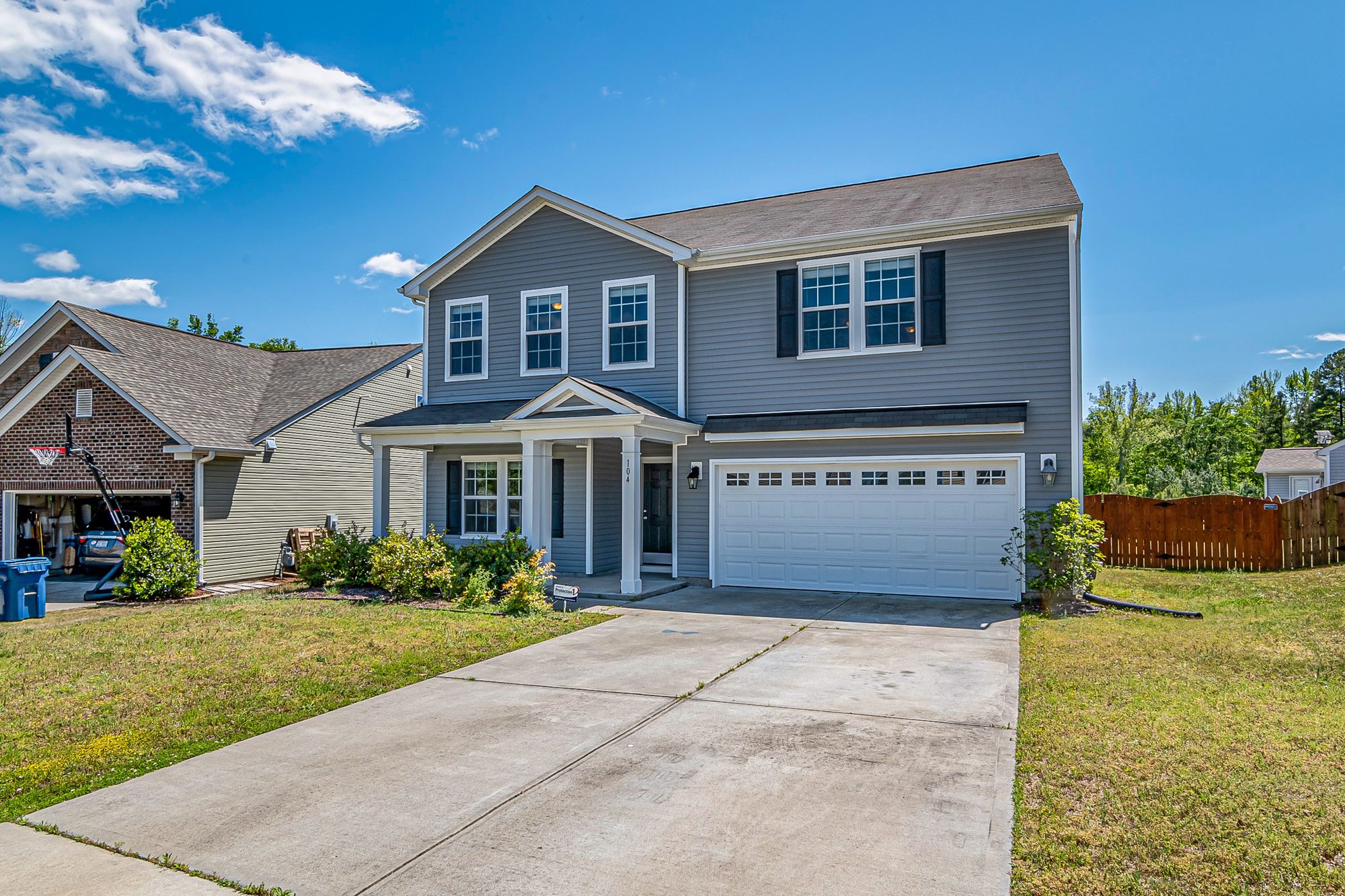 Two-car attached garage with white door and wide concrete driveway on a gray two-story home