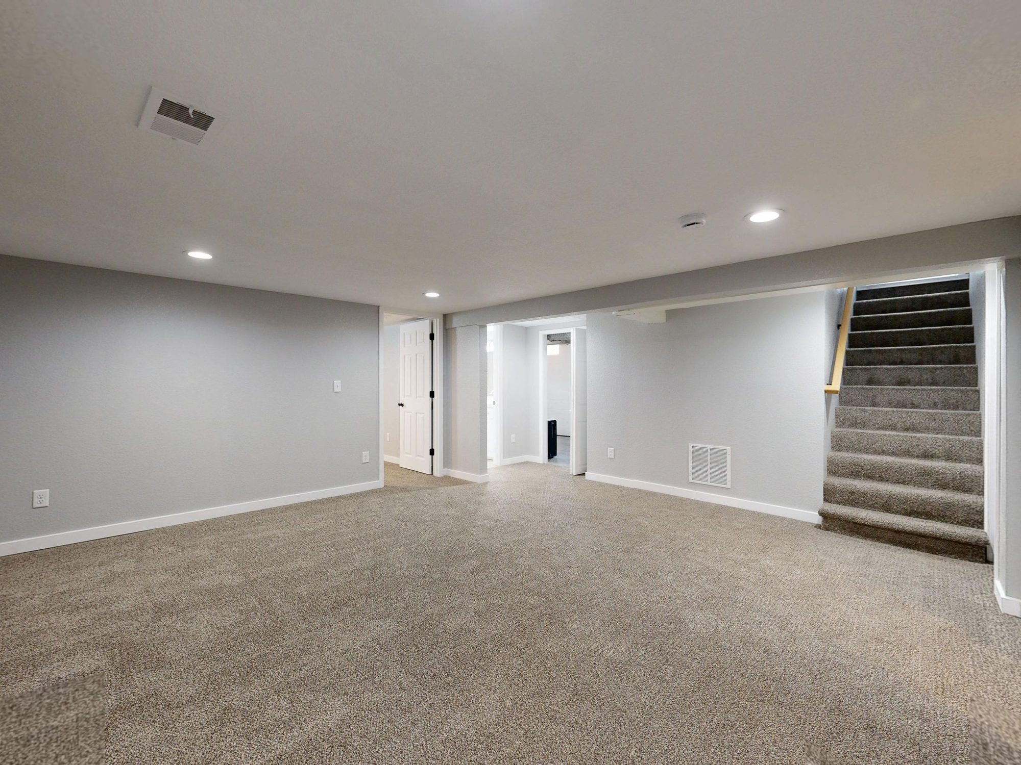 Bright finished basement with beige carpet, recessed lighting, white trim, and a carpeted stair