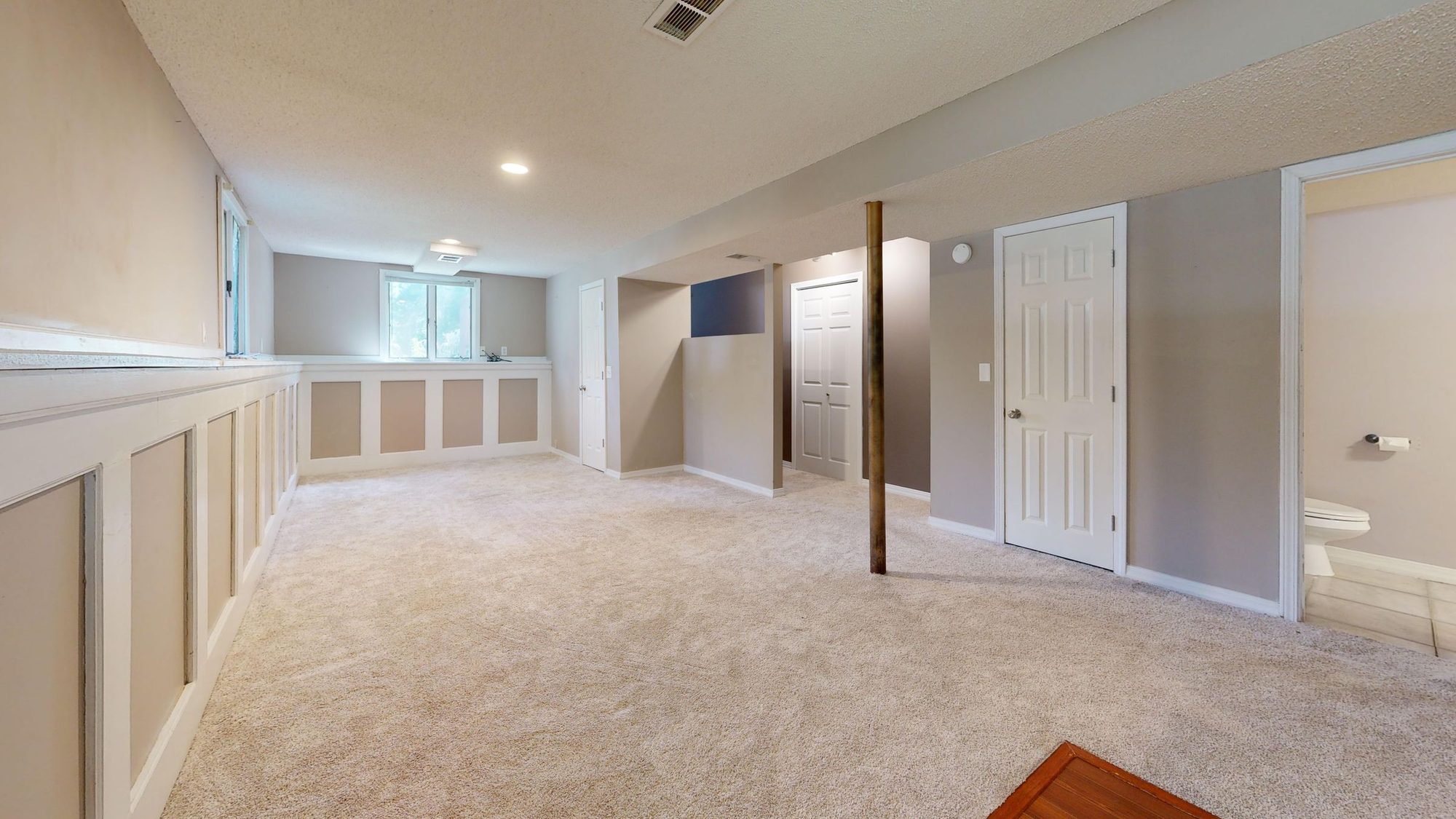 Bright finished basement family room with carpet, recessed lighting, wainscoting, and a door to a separate room