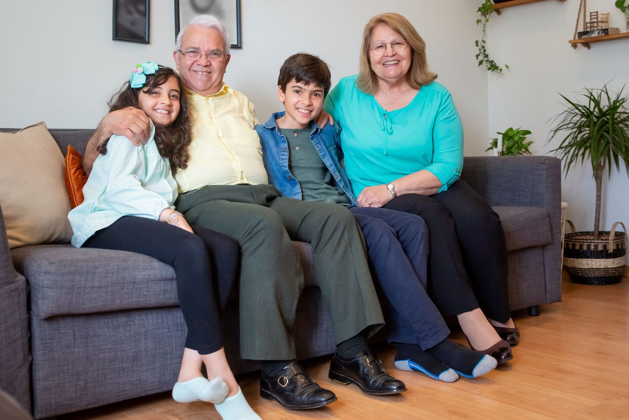 Grandparents and two grandchildren smiling together on a gray sofa at home