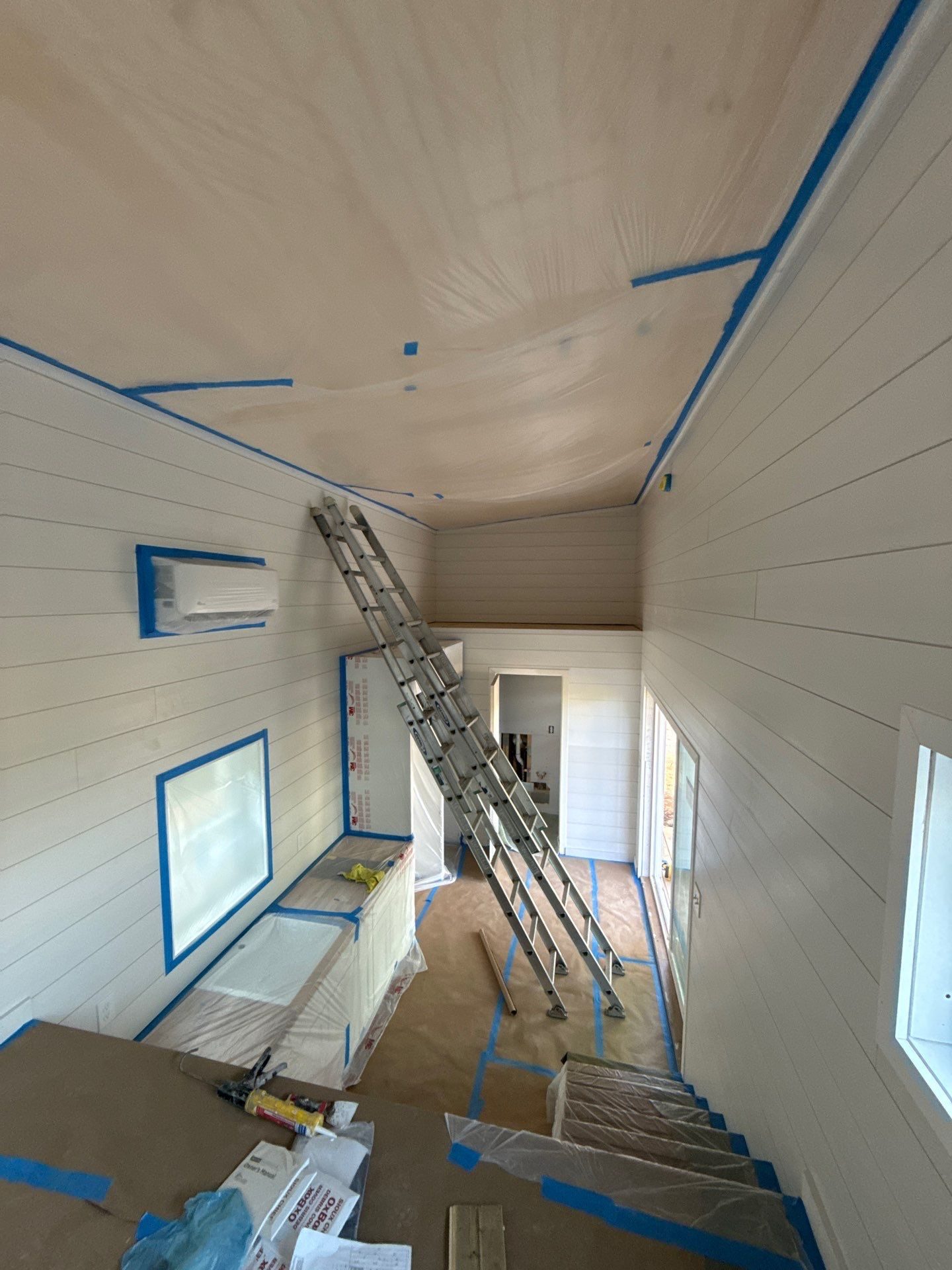 Peaceful Haven Homes backyard ADU under construction in Chattanooga with white shiplap walls, a mini-split, a loft ladder, stairs, and glass doors, masked for paint