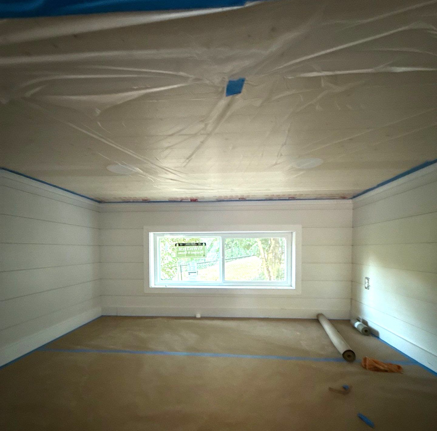 Shiplap-walled room with a wide window in a Peaceful Haven Homes backyard ADU under construction, floor papered and masked for paint