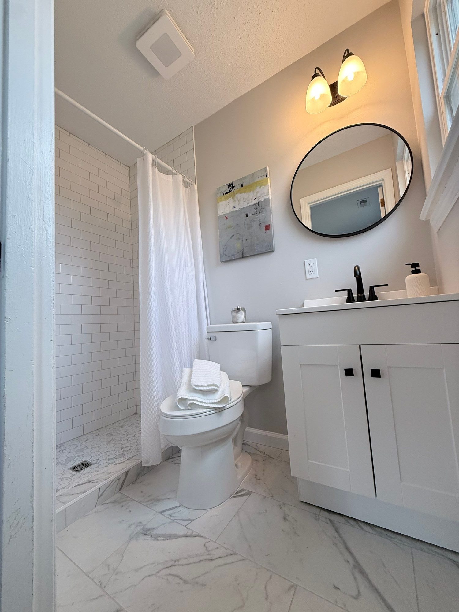 Bathroom in a lower-level mother-in-law suite finished by Peaceful Haven Homes, with a white subway-tile shower, round mirror, and white vanity