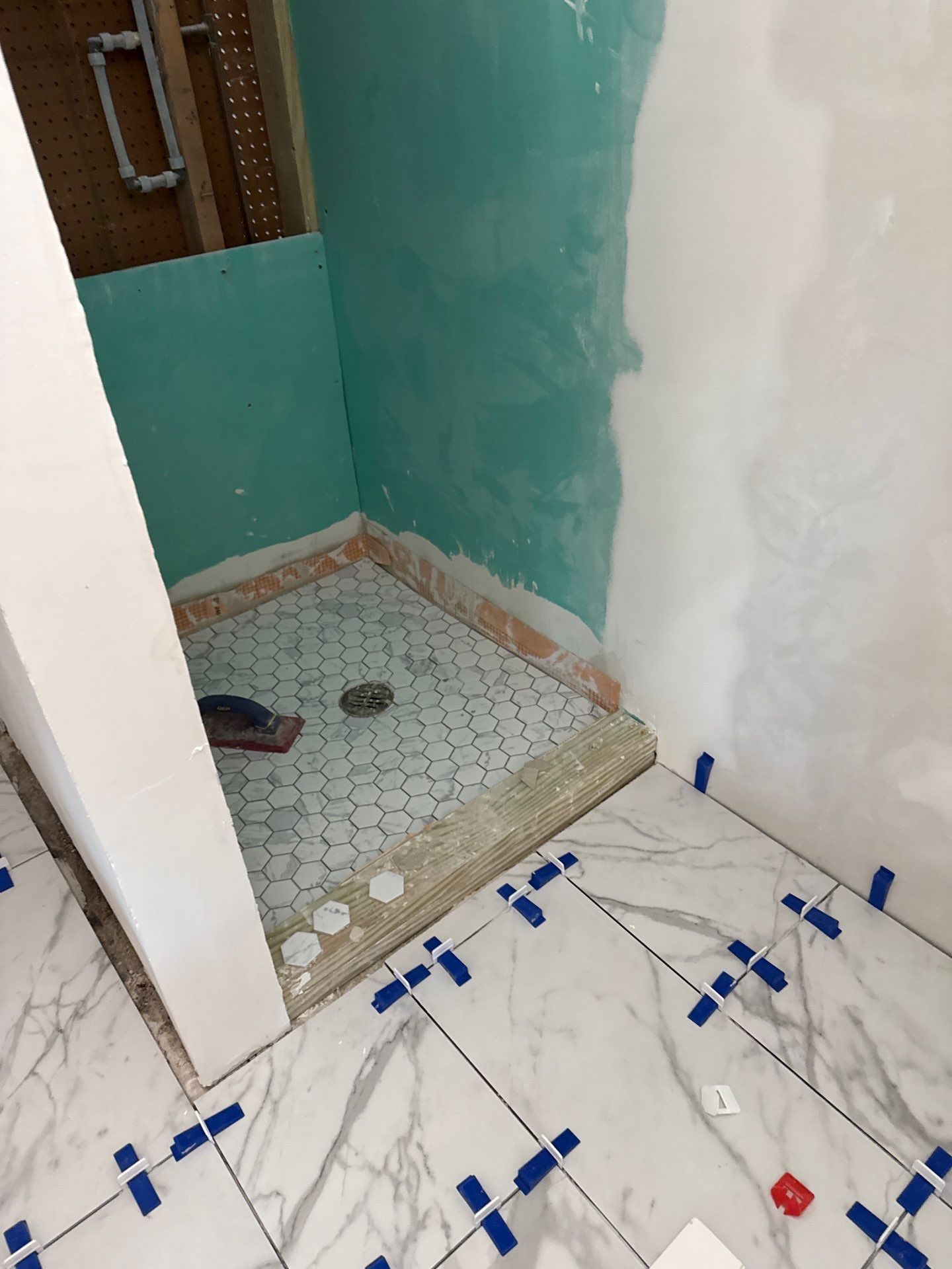Shower in progress in a lower-level mother-in-law suite by Peaceful Haven Homes, with moisture-resistant wall board, a hexagon mosaic shower pan, and marble-look floor tile set with leveling clips