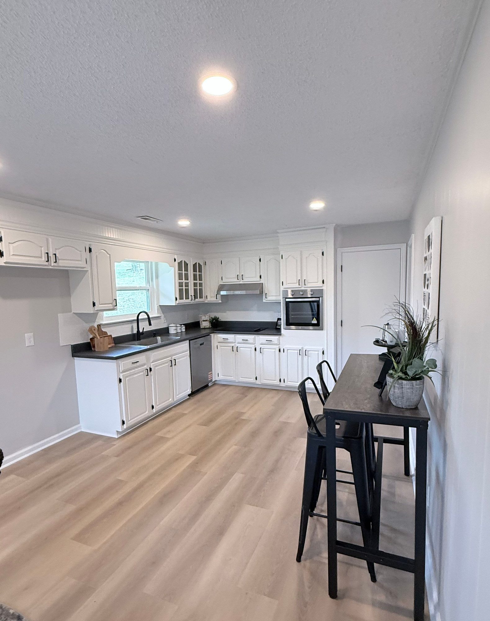 Kitchen in a Chattanooga lower-level mother-in-law suite finished by Peaceful Haven Homes, with white cabinets, dark countertops, a wall oven, and a high-top table