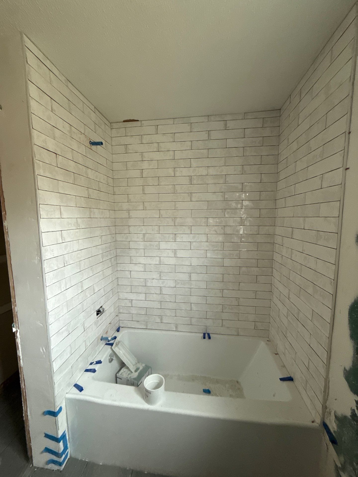 Lower-level suite bathroom tub with a new white subway tile surround before grout, by Peaceful Haven Homes