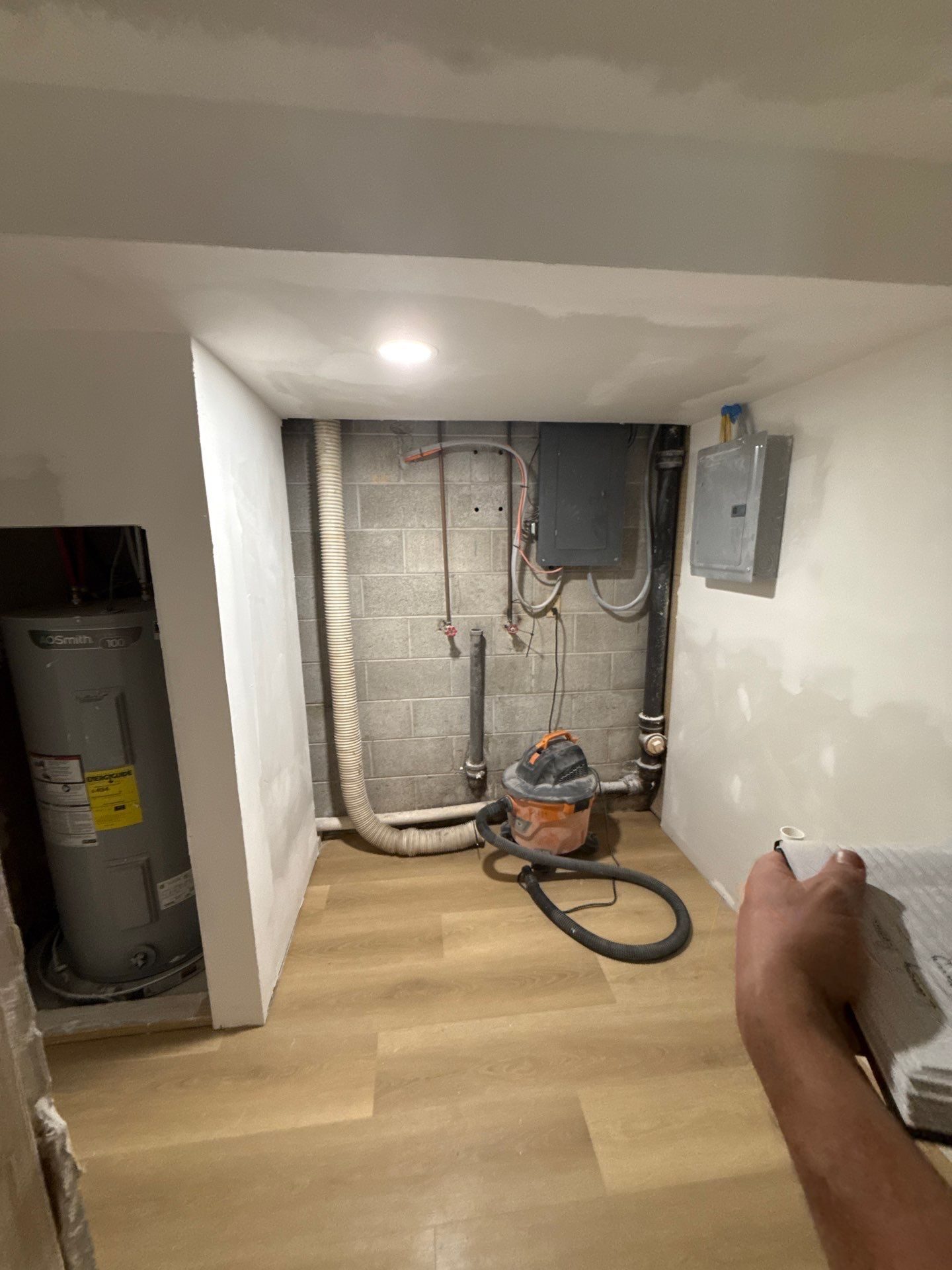 Utility room in a Peaceful Haven Homes lower-level suite with a water heater, electrical panel, exposed foundation wall, and new vinyl plank flooring
