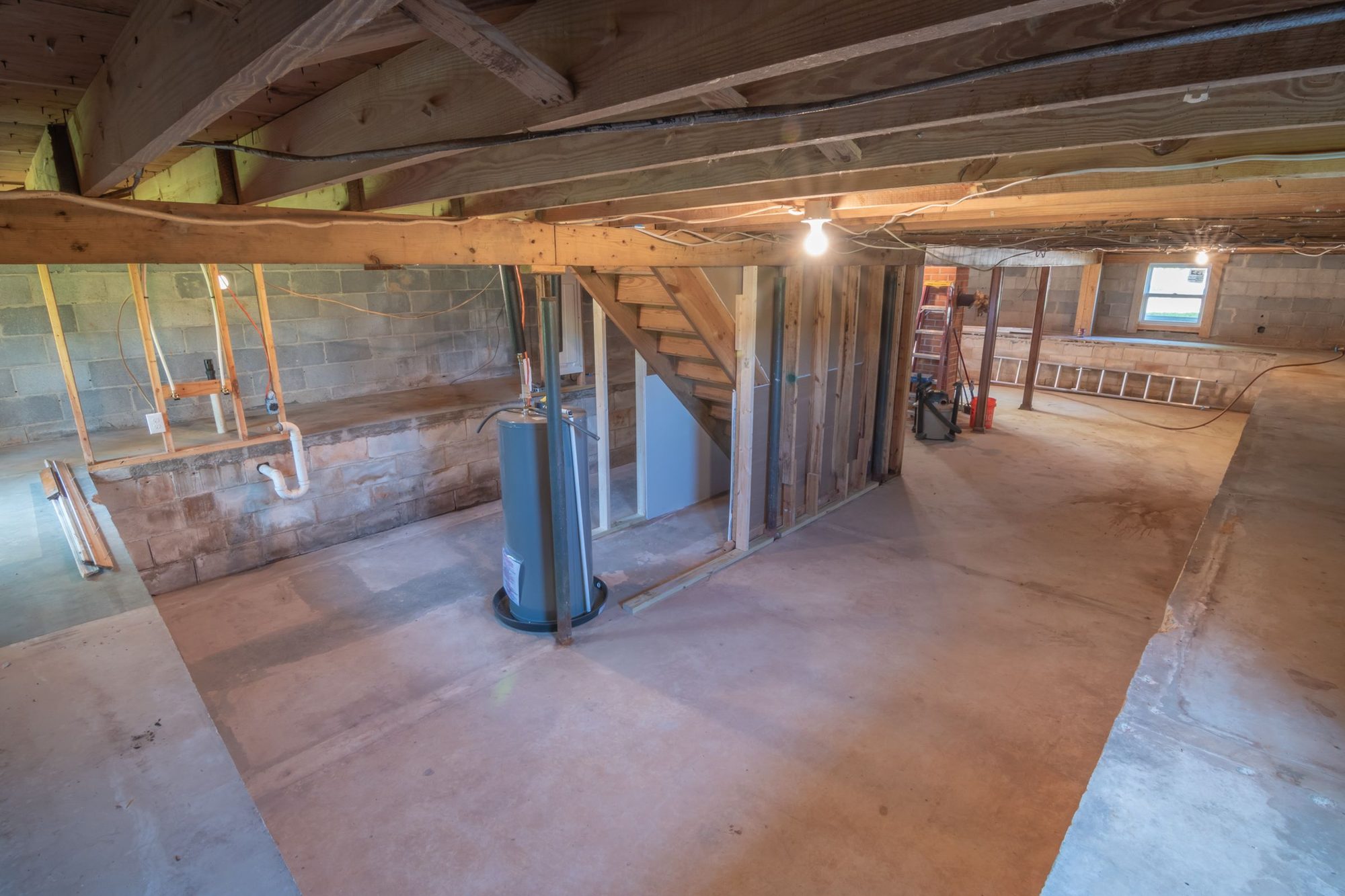 Unfinished basement with exposed floor joists, ductwork, plumbing lines, and a bare concrete floor